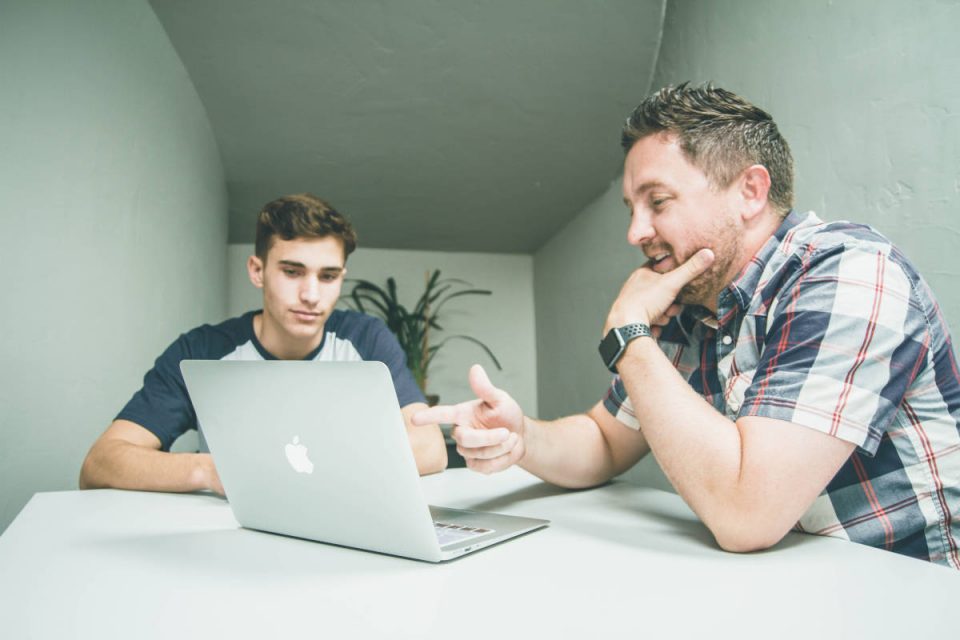 Mann zeigt jüngerem Mann etwas auf dem MacBook