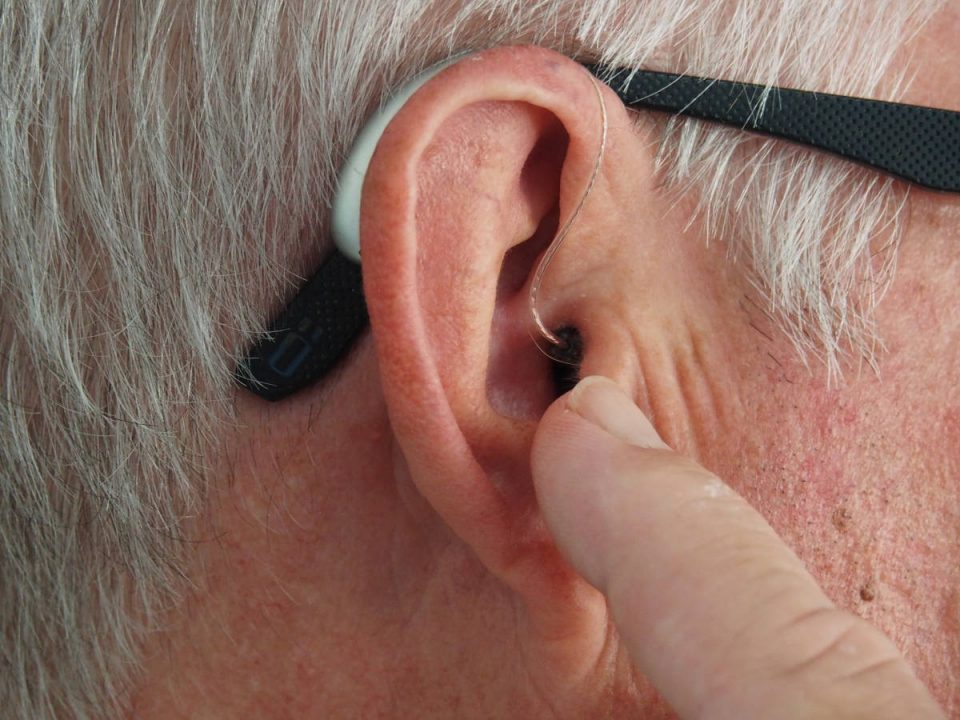 Mann trägt Brille und Hörgerät und zeigt auf sein Ohr