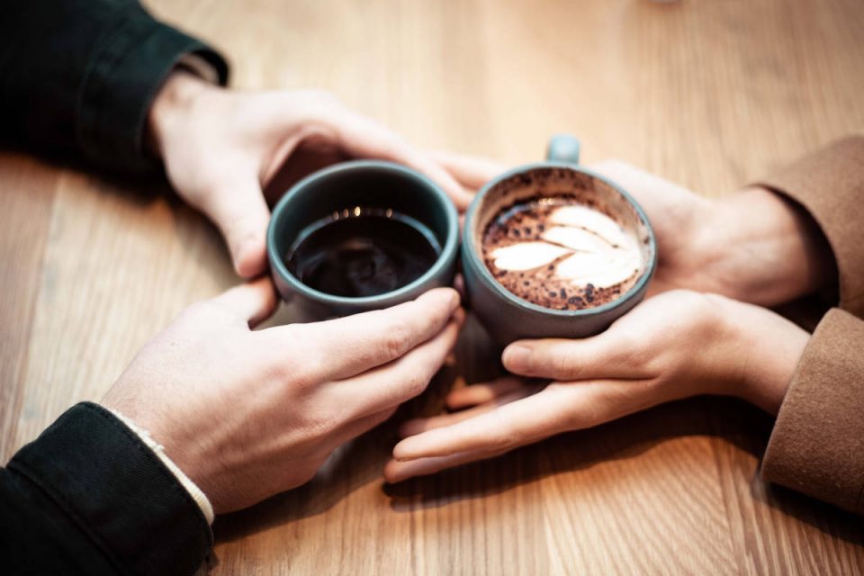 Zwei Menschen halten Keramik Kaffee Becher in der Hand und berühren die Hände des anderen