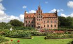 Braunes Steingebäude hinter Garten mit Wiese und Blumen